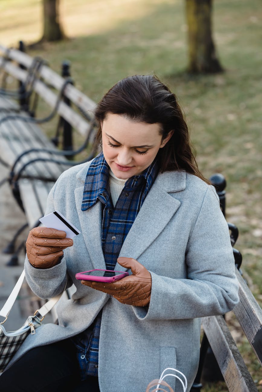 positive woman making online transfer via smartphone in park